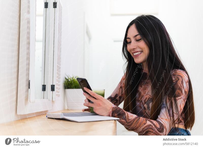 Woman on mobile phone taking notes in notebook and speaking on mobile phone sitting in bar with healthy beverage woman green smoothie take note write browsing