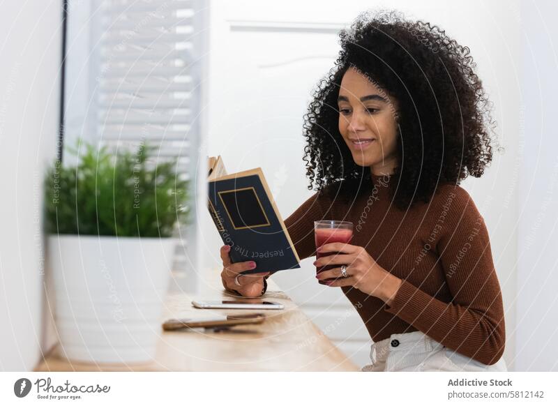 African American woman drinking smoothie and reading book in bar refreshment beverage summer chill female black african american ethnic smile relax rest glass