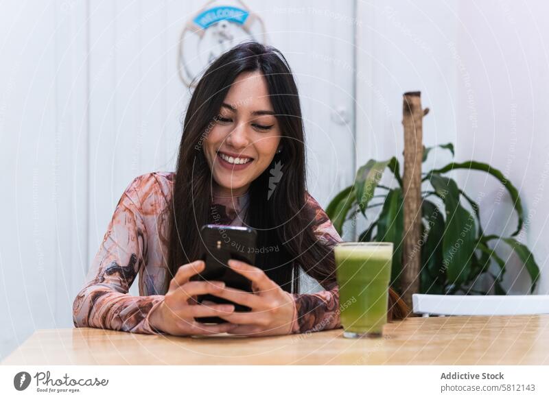 Smiling woman using smartphone at table in bar chill smoothie refreshment drink browsing beverage female mobile device internet rest happy gadget alcohol