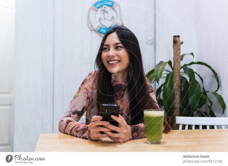 Smiling woman using smartphone at table in bar chill smoothie refreshment drink browsing beverage female mobile device internet rest happy gadget alcohol