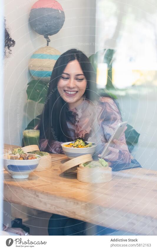 Smiling woman eating in restaurant while using mobile phone women together friend smartphone share spend time friendship food female cheerful happy browsing