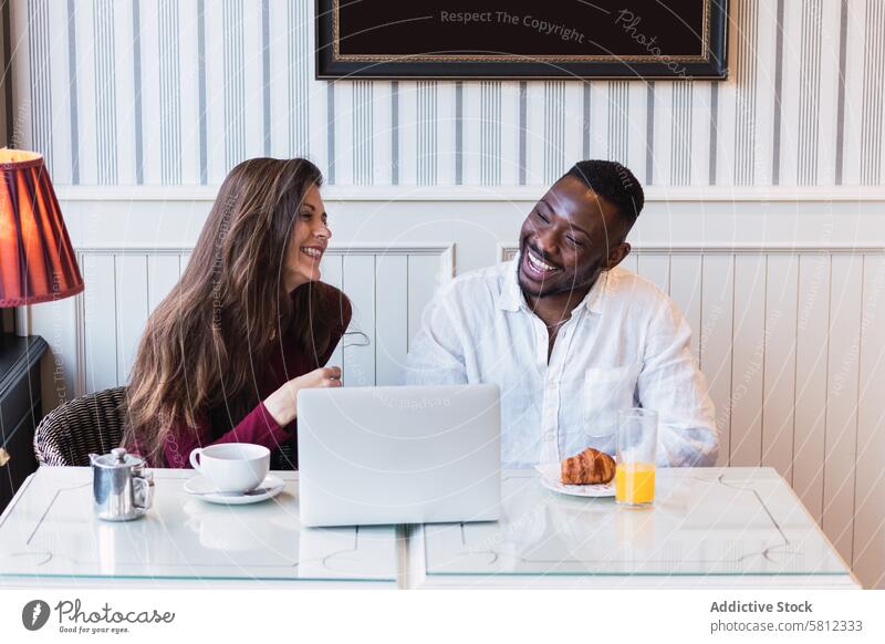 Cheerful multiethnic couple using laptop during breakfast at home together happy relationship cheerful browsing watch multiracial diverse black african american