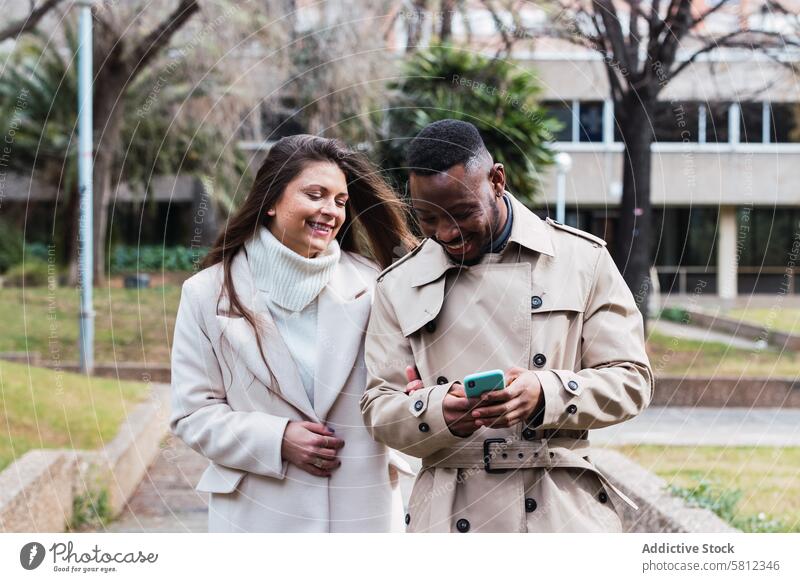 Joyful multiethnic couple using smartphone in park happy together mobile romantic love content adult multiracial diverse african american black news