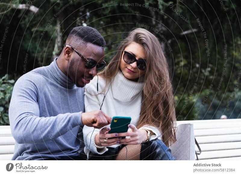 Joyful multiethnic couple listening music on smartphone in park using happy together mobile romantic love adult multiracial diverse african american black news