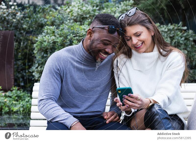 Joyful multiethnic couple listening music on smartphone in park using happy together mobile romantic love adult multiracial diverse african american black news