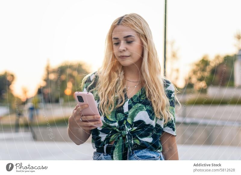 Blonde girl using mobile phone outdoors happy young summer woman female people leisure lifestyle joyful looking spring enjoyment hair city cool stylish outfit