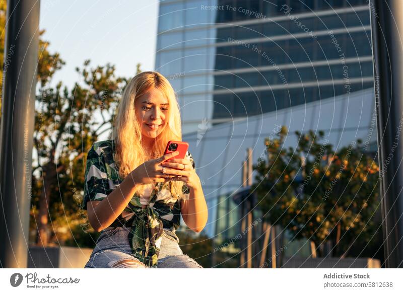 Blonde girl using mobile phone outdoors happy young summer woman female people leisure lifestyle joyful looking spring enjoyment hair city cool stylish outfit