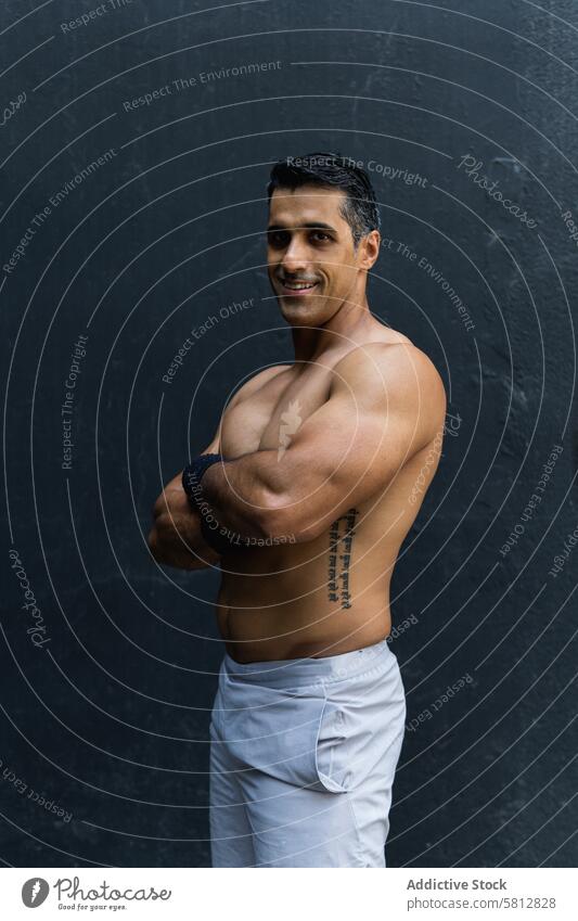 Positive shirtless Hispanic sportsman near wall training healthy lifestyle wellness fitness muscular naked torso content street male arms crossed serious