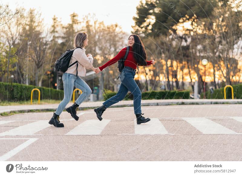 two student girls crossing crosswalk holding her hands, running and smiling street people road city traffic urban child female pedestrian person safety zebra