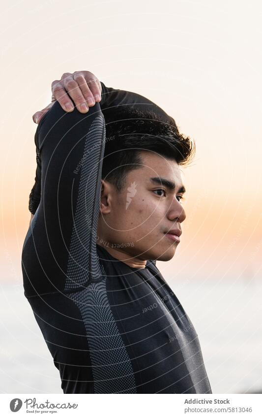 Ethnic sportsman stretching shoulders near sea workout fitness arm training exercise sporty sunset warm up asian ethnic male lifestyle athlete wellness young