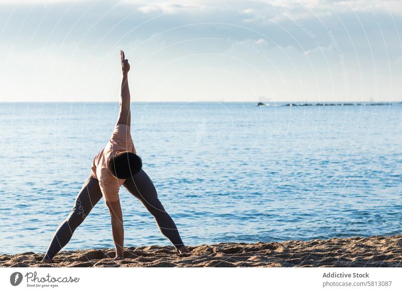Flexible man doing twisted yoga asana near sea beach revolved wide legged forward bend pose practice stand balance male lifestyle wellness wellbeing vitality