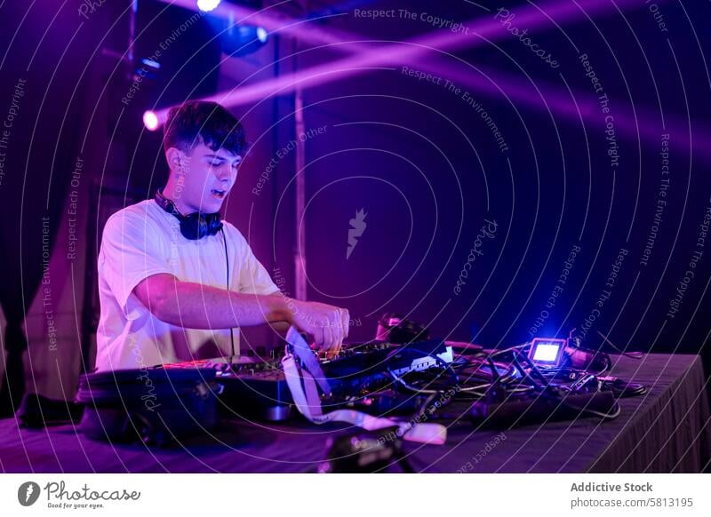 Young DJ working on mixing board man young dj disco male casual purple neon lights night music entertainment club dance turntable party groove beats spin