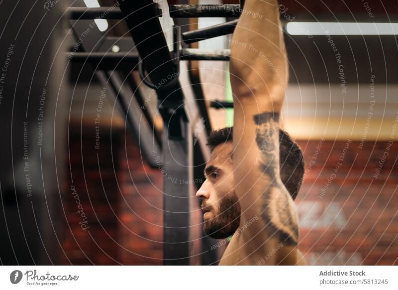 side view of a strong man doing pull ups in a gym. close-up training exercise fitness male workout sport physical healthy strength lifestyle athletic muscular