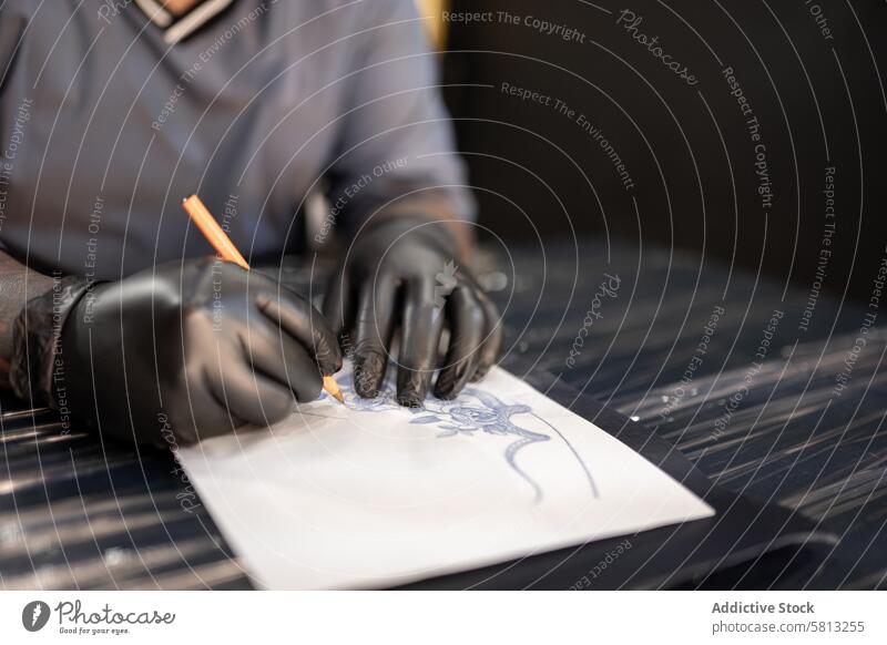 A tattoo artist is drawing a design stencil on his work stretcher before tattooing young adult hispanic latino pencil professional sweatshirt protection hygiene