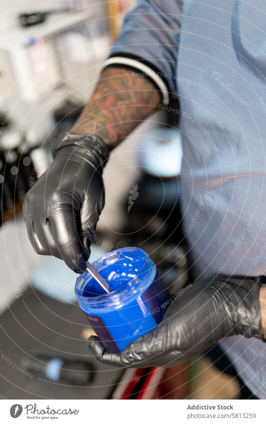 A tattoo artist is picking up some blue skin vaseline before work young adult hispanic latino professional sweatshirt protection hygiene safety tape glasses