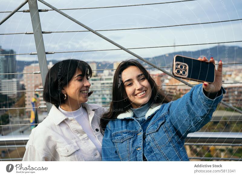 Joyful friends taking a selfie with cityscape background smartphone joy happiness togetherness urban outdoor leisure casual clothing denim jacket youth