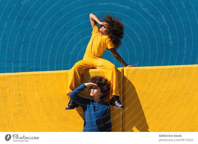 Black curly haired girl and boy resting near colorful wall kid afro together bright vivid hairstyle teen friend african american black ethnic sibling yellow