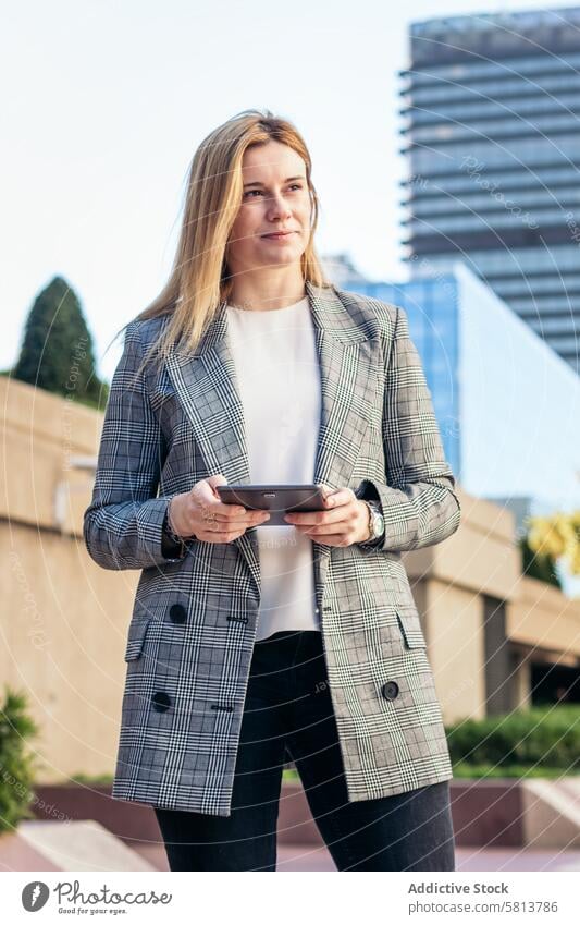 Focused blonde business woman in a suit using a tablet outside and smiling meeting team professional executive success entrepreneur finance businesswoman