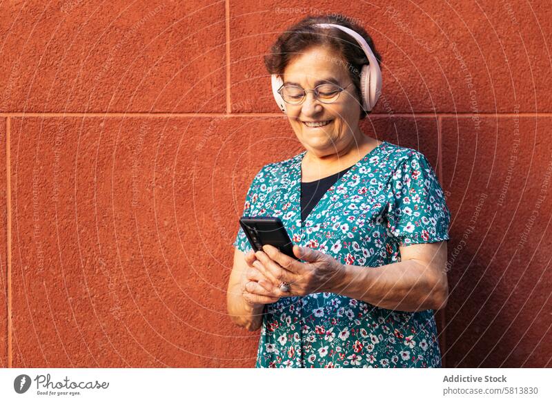 Old woman using smartphone and listening to music with headphones stylish mobile cellphone senior female communication device message lifestyle internet