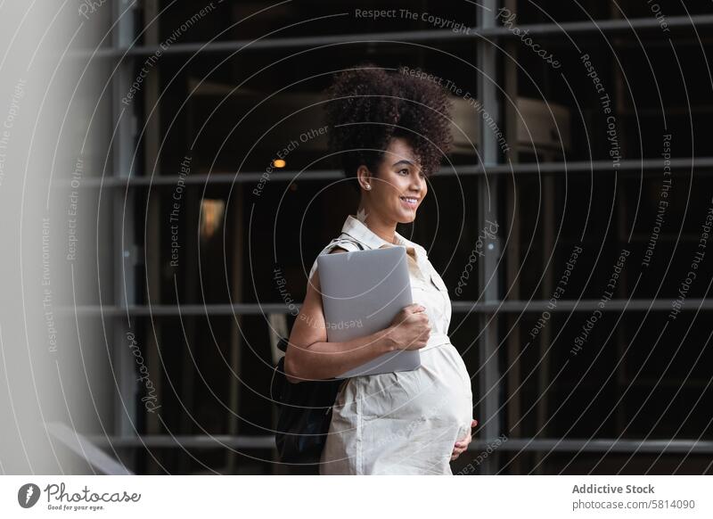 Smiling black woman with laptop coming out of office building pregnant carry maternal anticipate expect tower happy female tummy gadget device belly digital