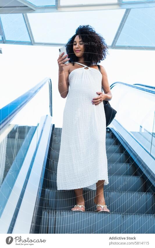 Pregnant black woman browsing smartphone on escalator pregnant using belly connection anticipate online female await pregnancy expect motherhood maternal