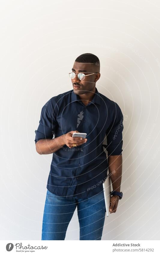 Thoughtful black guy with phone and laptop near white wall man smartphone serious well dressed modern eyeglasses studio shot netbook african american male adult