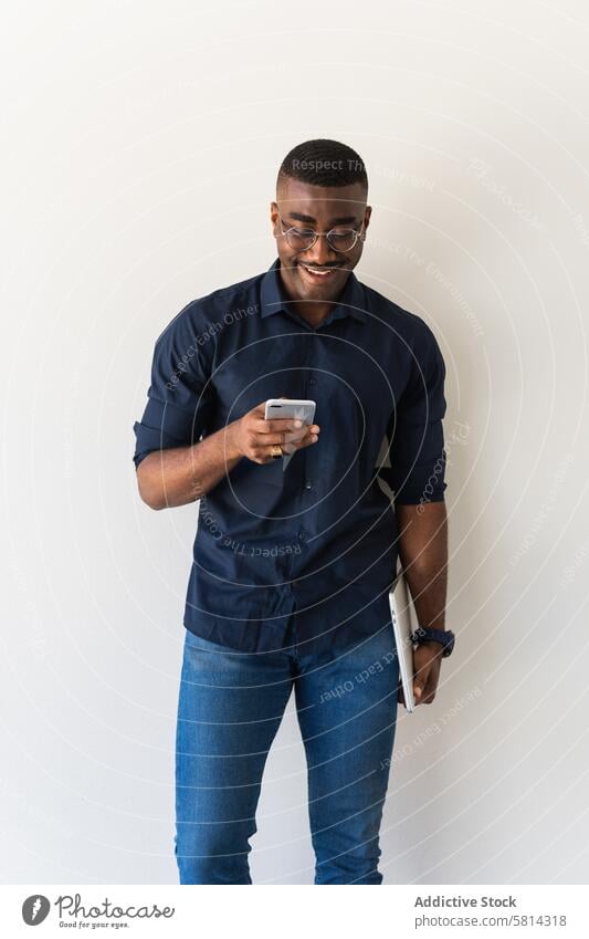 Happy black guy with phone and laptop near white wall man smartphone well dressed modern eyeglasses studio shot netbook african american male adult shirt