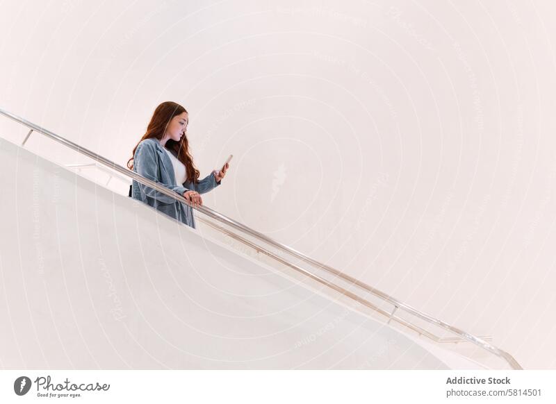 Woman browsing smartphone on staircase woman online text message stairway chat style modern elegant design corridor hall fashion female trendy app social media