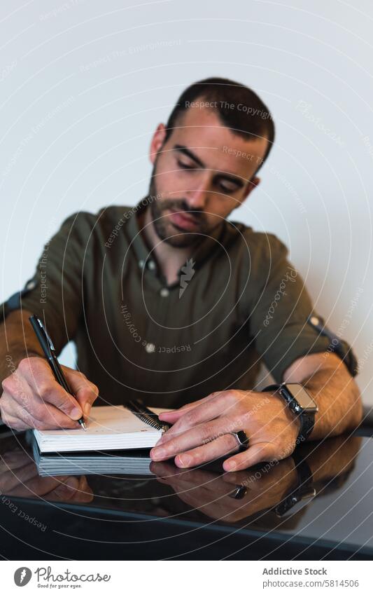 Man writing in notebook near laptop man take note notepad write work workplace reminder task male table device modern guy room planner light organizer pen