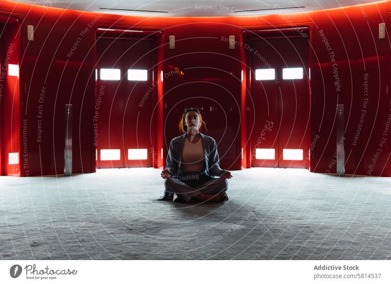 Woman meditating in foyer with elevators woman lobby lotus pose zen lift meditate stress relief obscure design feminine glow dark red spacious trendy modern dim