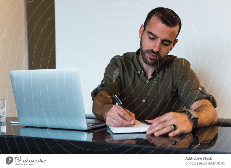 Man writing in notebook near laptop man take note notepad write work workplace reminder task netbook male table device modern guy room planner light organizer