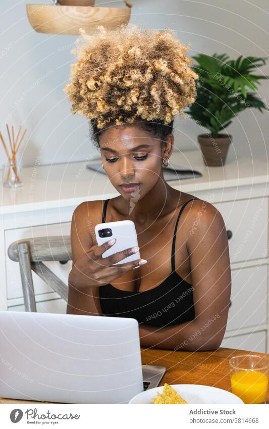 Black serious female freelancer using smartphone at table with breakfast woman watch laptop morning internet juice gadget browsing connection online concentrate