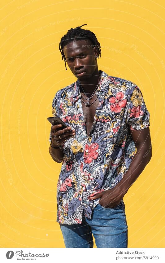 Stylish black man in colorful shirt with smartphone style trendy summer hipster fashion using confident young african american ethnic male floral jeans mobile