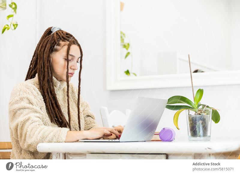 Thoughtful woman with dreadlocks working with a laptop at home computer sitting room internet female technology people lifestyle young girl house modern