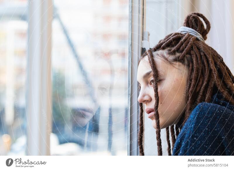 Pensive woman with dreadlocks looking out the window pensive home people thinking braids contemplation beautiful portrait person adult lifestyle face female