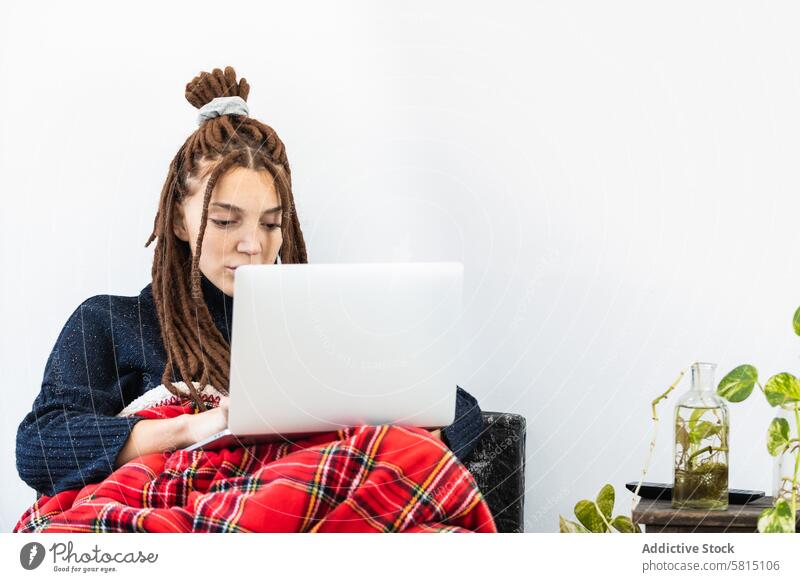 Woman with dreadlocks working with a laptop at home woman computer sofa sitting room internet female technology people lifestyle young girl house couch modern