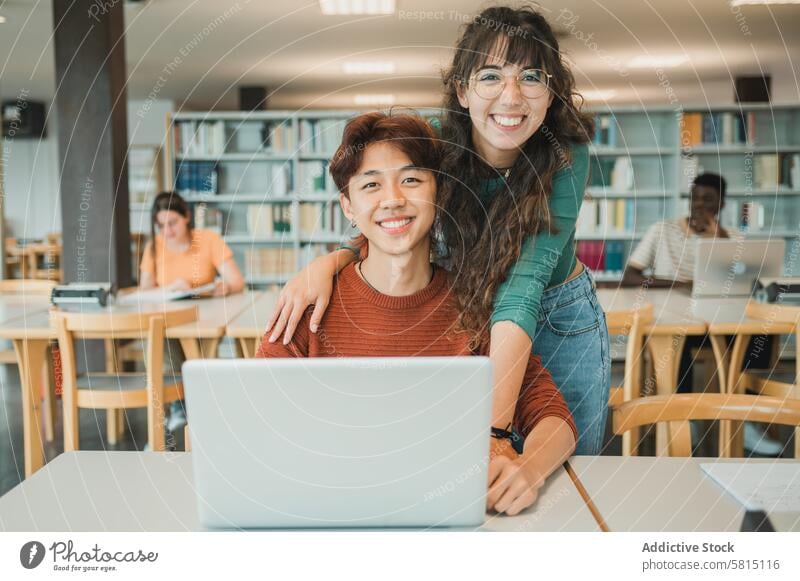 Cheerful diverse students with laptop in library friend smile study university together portrait hug education teen young adolescent teenager happy homework