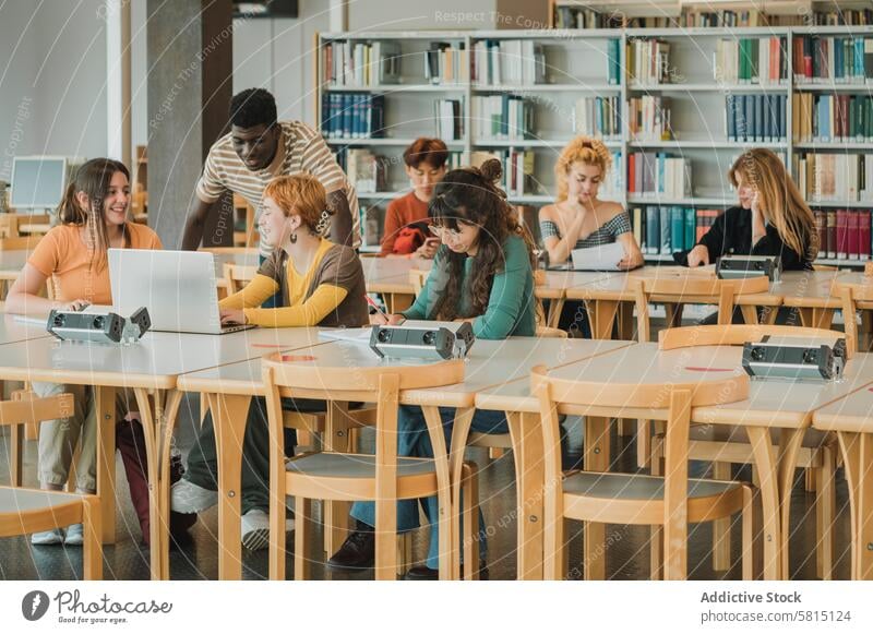 Multiethnic students doing homework in modern library classmate talk study together university education learn knowledge lean table laptop research speak gadget