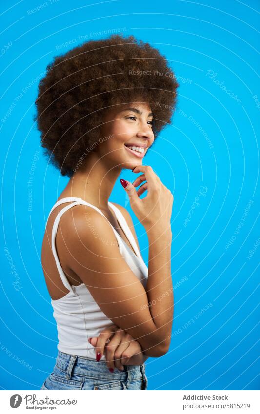 latina woman with afro hair in profile with hand on chin smiling studio photo with blue background portrait female young person face beauty happy adult model
