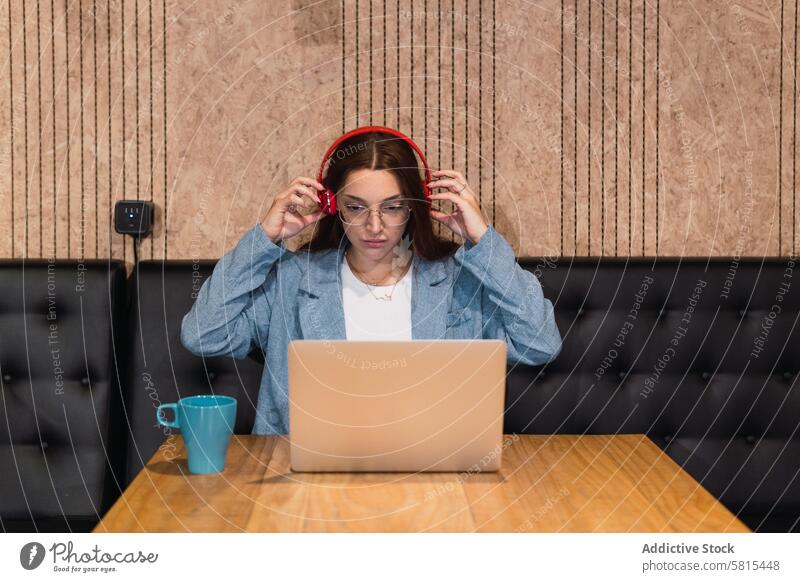 Female freelancer putting on headphones businesswoman put on prepare cafe serious laptop remote table female young hot drink listen music wireless headset
