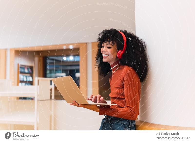 Glad African American female listening to music from laptop woman library using melomaniac student headphones smile stand browsing education enjoy ethnic