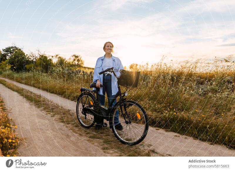 blonde woman standing with a bike in a field at sunset bicycle young girl fashion summer nature pretty countryside female lifestyle travel beautiful happy grass