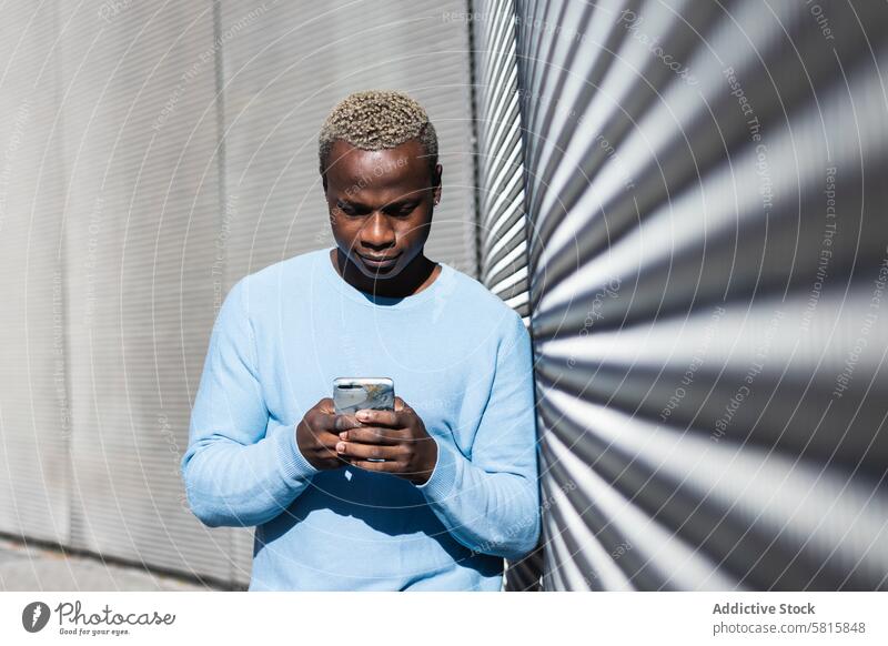 Young black guy browsing smartphone on street man joy watching texting happy optimist male young ethnic african american dyed hair casual city social media