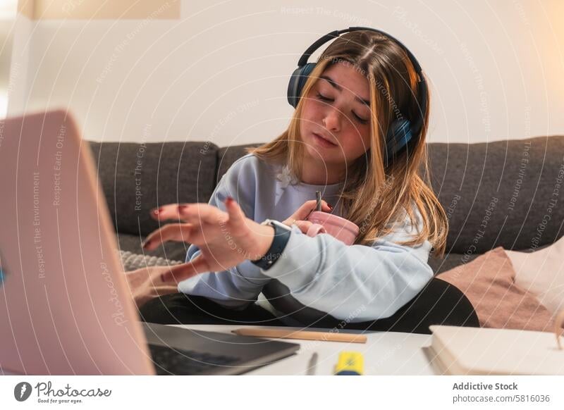 Young woman multitasking while working from home young headphones laptop confused puzzled expression female technology sofa living room indoor casual
