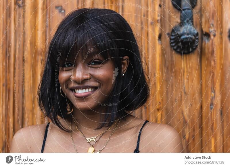 Cheerful black woman in black outfit against wooden wall cheerful happy smile positive glad fun carefree female hand on waist bright pleasure delight joy