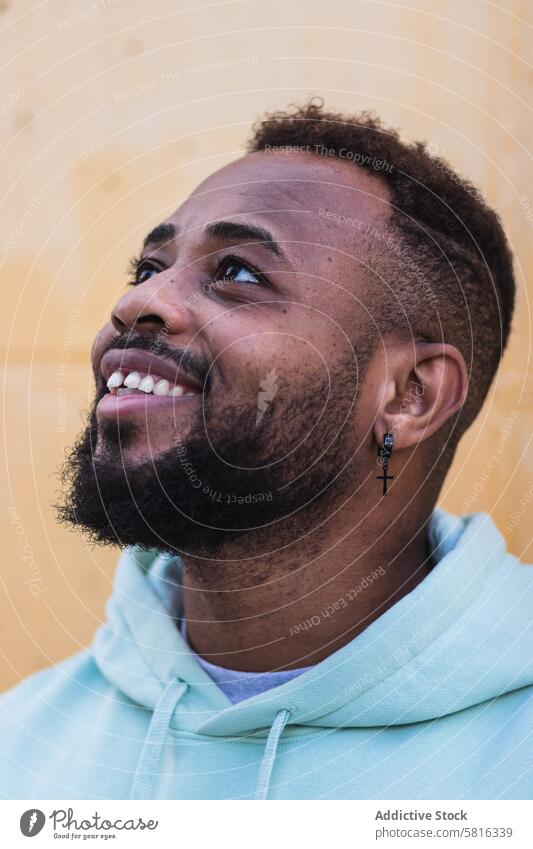 Cheerful black man in hoodie standing near wall cheerful happy hipster urban laugh trendy positive beard tooth cool adult african american ethnic male casual