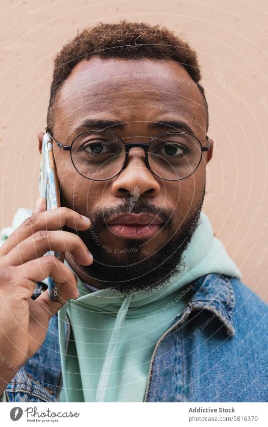Black man talking on phone near wall smartphone hipster casual conversation communicate adult african american black ethnic beard male satisfied device