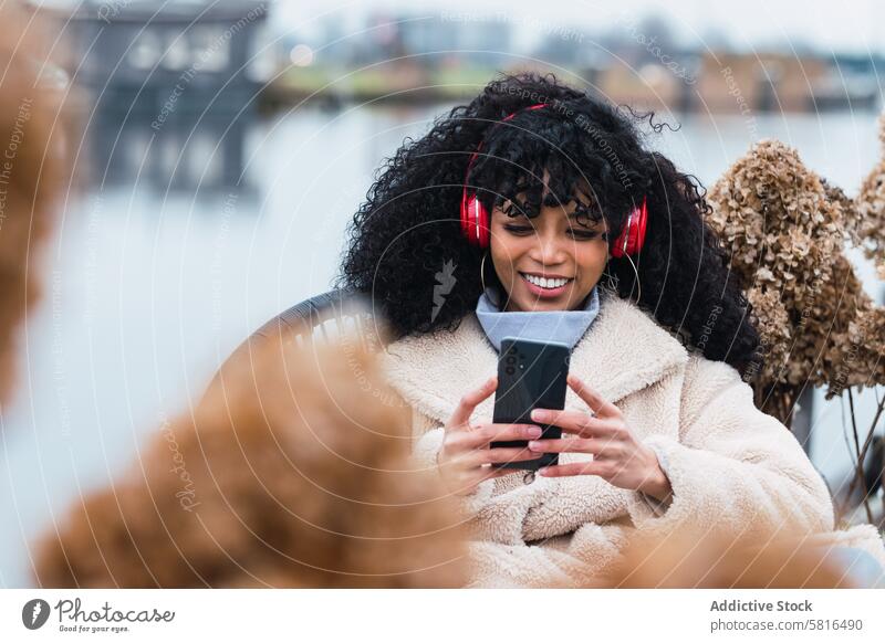 Cheerful black woman listening to music at lakeside headphones smartphone using chill rest relax park female african american woman city smile positive urban