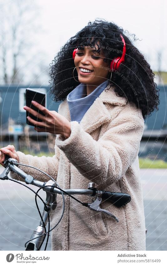 Delighted black woman with smartphone on bicycle headphones using music listen ride bike chill female walk african american woman relax city portrait street