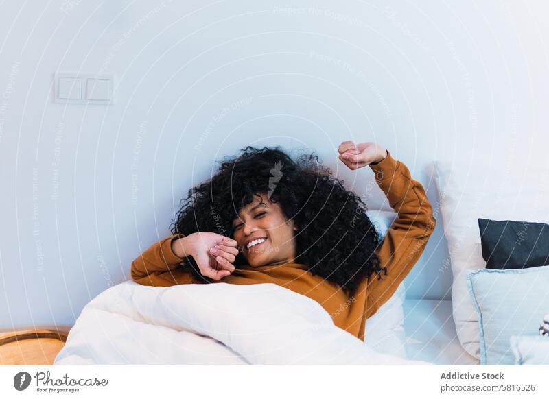 Smiling black woman waking up in bed wake up awake morning stretch weekend at home relax rest female african american eyes closed bedroom smile happy young